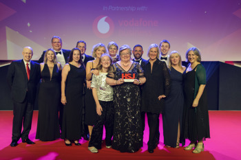 A group of people on stage at an award show. The person is the middle is holding an award.